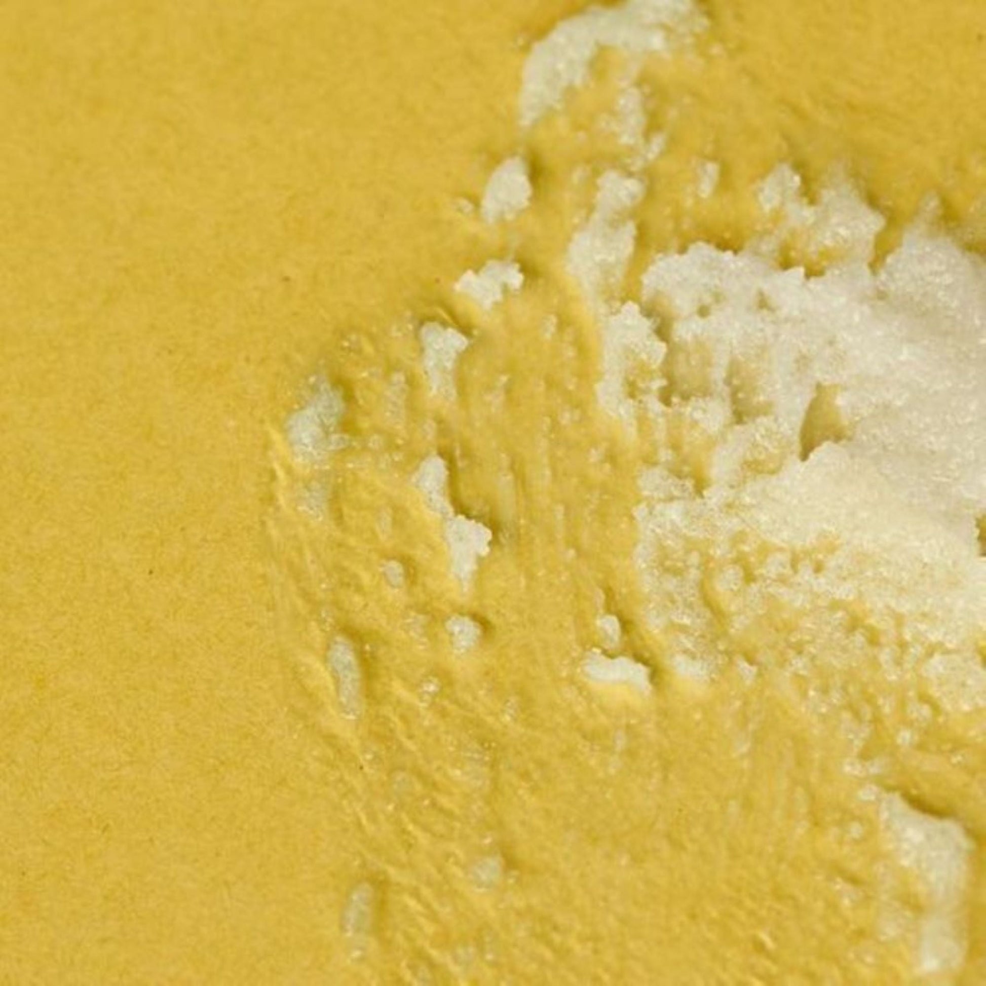 H. Honeycup body scrub smeared on yellow background to show sugar texture