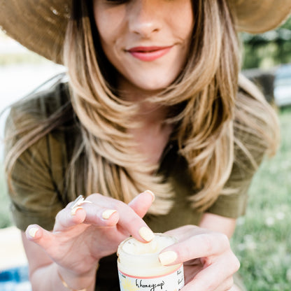 Woman outside dipping finger in H. Honeycup body scrub