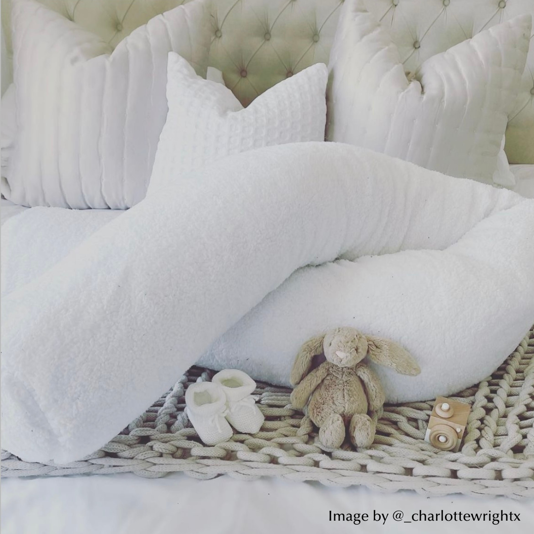 White pregnancy pillow on a bed with baby toys and booties